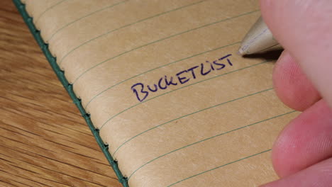 closeup of hand writing bucket list into blank notebook