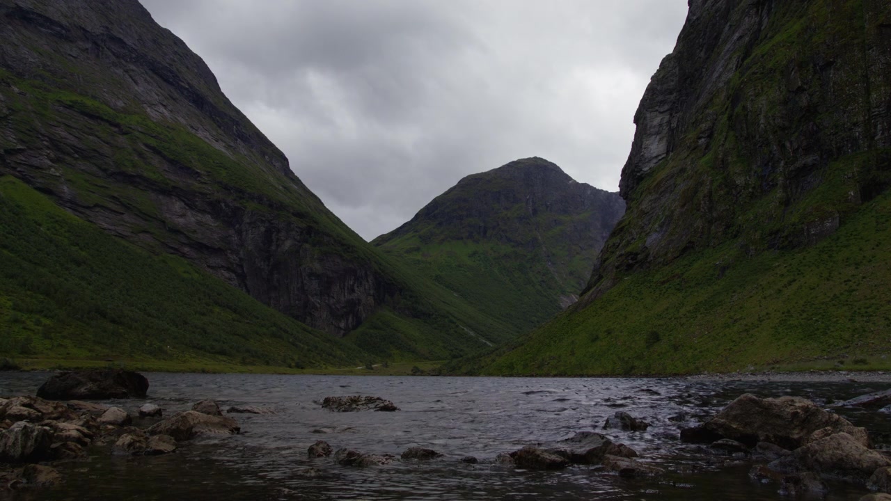 Acqua bassa del fiordo simile a un fiume si increspa tra ripide pareti rocciose verdi nella Valle di Norangsdalen sotto un cielo grigio