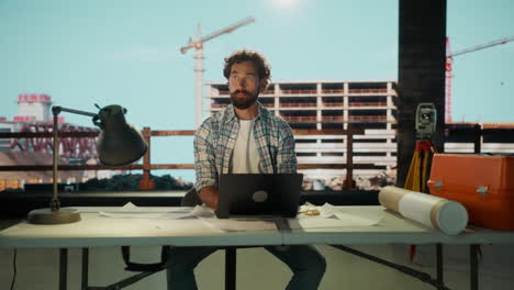 engineer or architect working on laptop and blueprints at a construction site