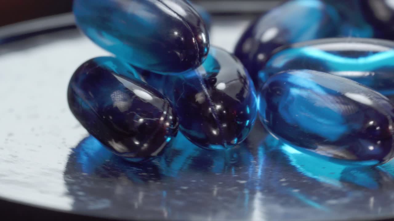 Blue gel medicine capsules rotating on reflective metallic surface, studio close up shot