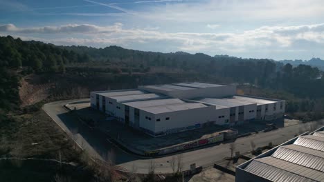 Industrial-warehouses-near-Abrera,-Barcelona,-Spain,-surrounded-by-greenery,-aerial-view