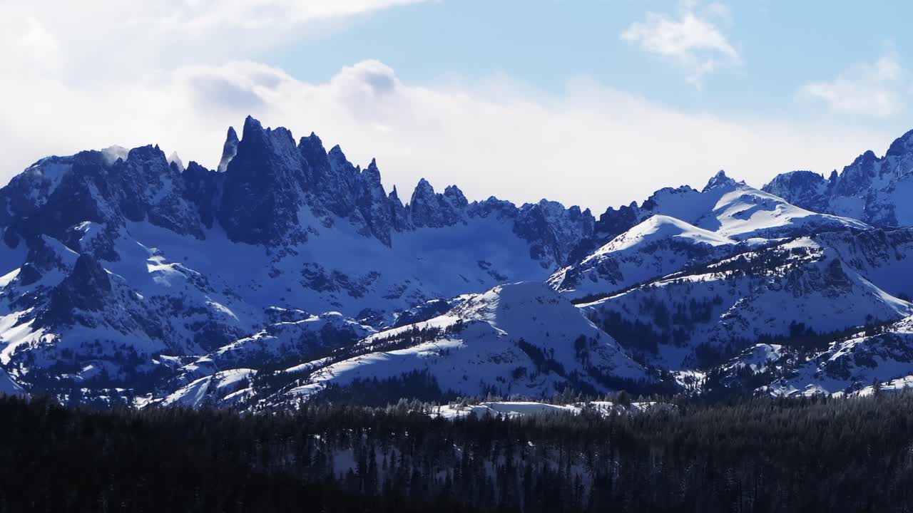 The Hemlocks Mammoth Mountain ski snowboard resort aerial drone parallax right California The Minarets jagged towering peaks winter sunny blue sky afternoon fresh deep snow clouds Inyo National Forest