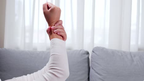 woman is raising her hand to massage and clench her sore wrist on the sofa, using her hands to massage herself to relieve pain and improve symptoms