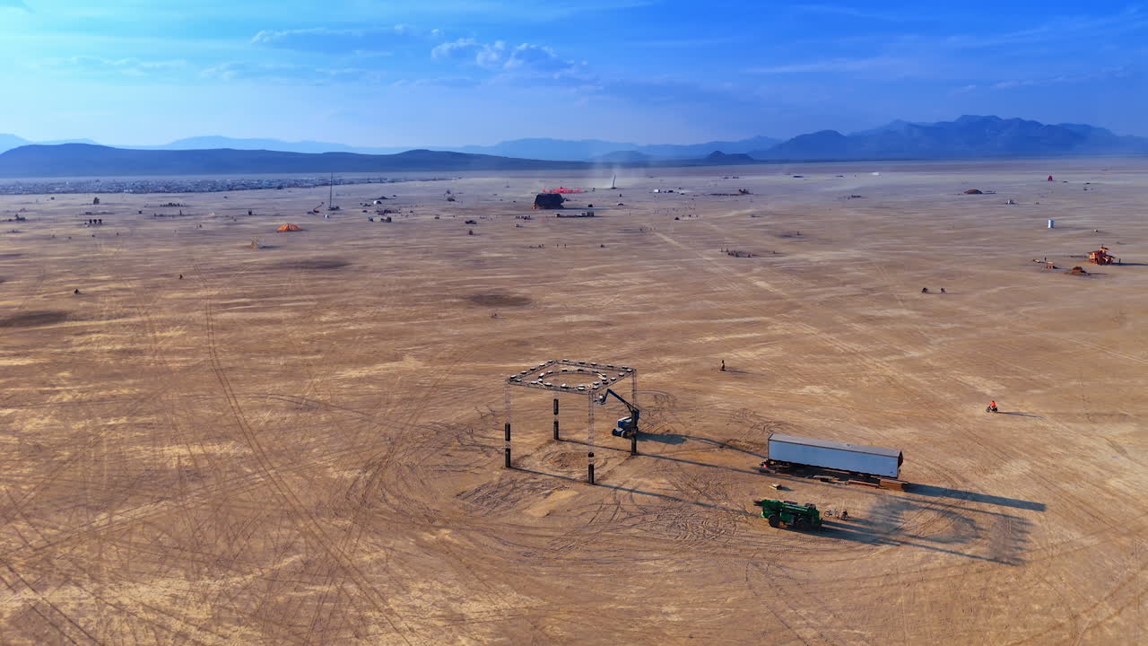 Drone view of a large desert art installation surrounded by open playa with festival camps in the background