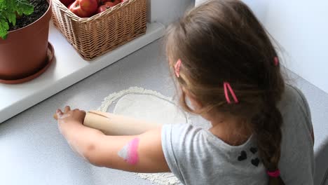 high angle, no face of brunette little girl stretch the dough with a rolling pin for pizza recipe