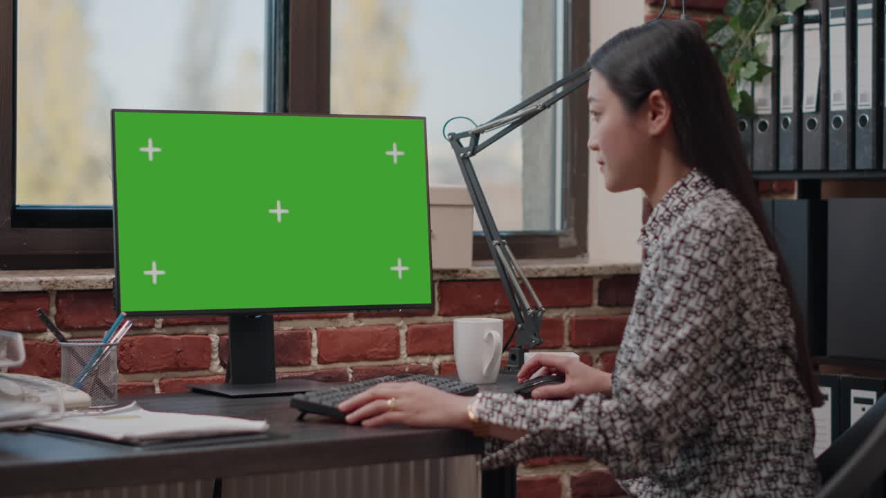 Asian woman working on monitor with horizontal green screen