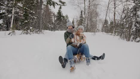 dolly shot of happy young women friends sledding down the mountain in winter wood laughing