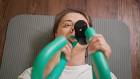 woman bends butterfly expander on floor closeup. strong lady works upon arms muscles lying on mat in home gym. equipment of hands development