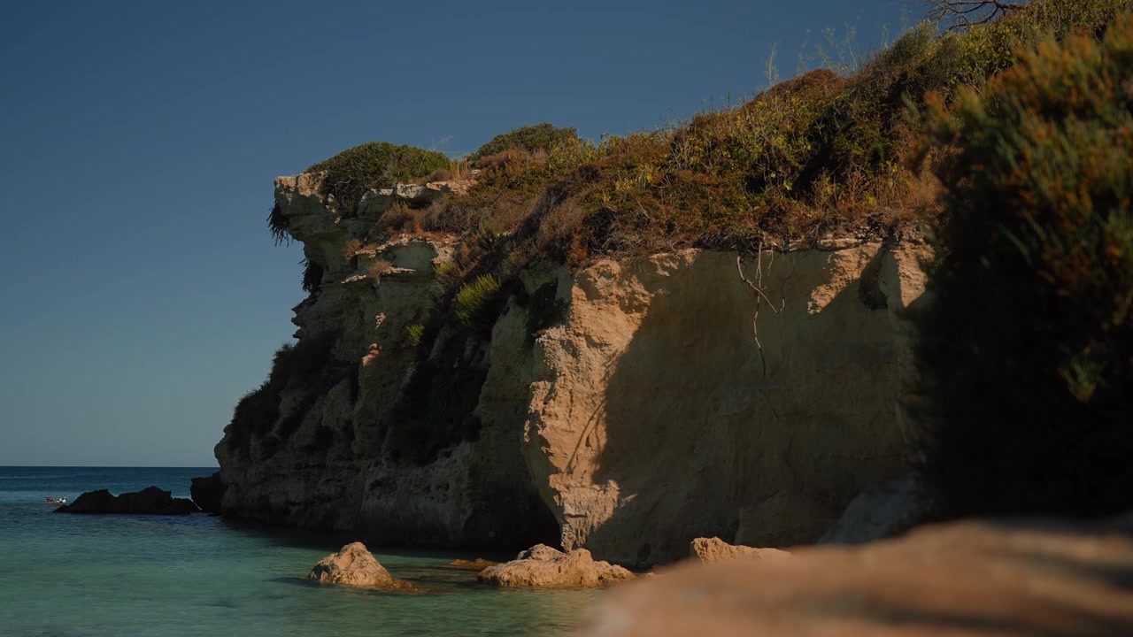 Drammatiche scogliere calcaree si ergono sopra acque cristalline del Mediterraneo con vegetazione lussureggiante sulla cima della scogliera.