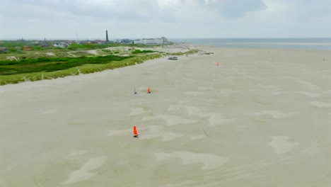 colorful land yachts sail over vast sandy flats by borkum’s shore under overcast skies. aerial orbit view