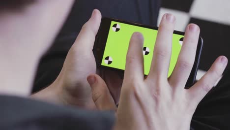 person holding a smartphone with a green screen