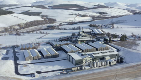 Vista-Aérea-De-La-Destilería-De-Whisky-Glenlivet-Rodeada-De-Nieve-Al-Sol-De-La-Tarde-En-Un-Día-De-Invierno,-Moray,-Escocia---Tiro-De-Avance