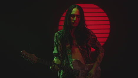 indie musician playing electric guitar with eyes closed in dark studio
