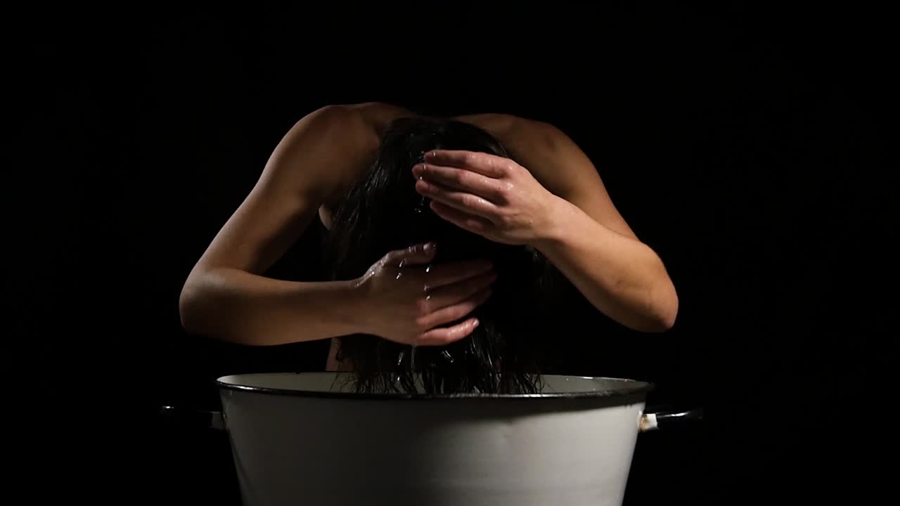 Woman wash her hair on white metal barrel with naked body on black studio background centered