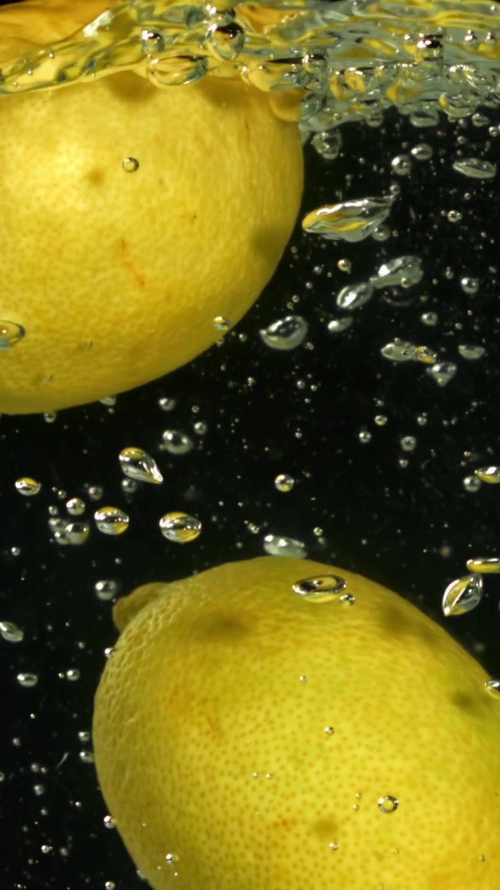 Limoni freschi immersi nell'acqua con bolle su sfondo nero