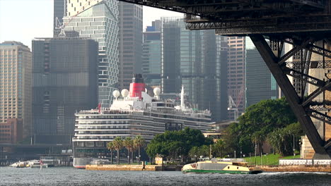 A-ferry-passes-under-Sydney-harbour-bridge-with-a-large-cruise-ship-in-the-background