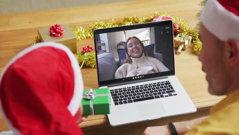 Caucasian-father-and-son-with-santa-hats-using-laptop-for-christmas-video-call-with-woman-on-screen