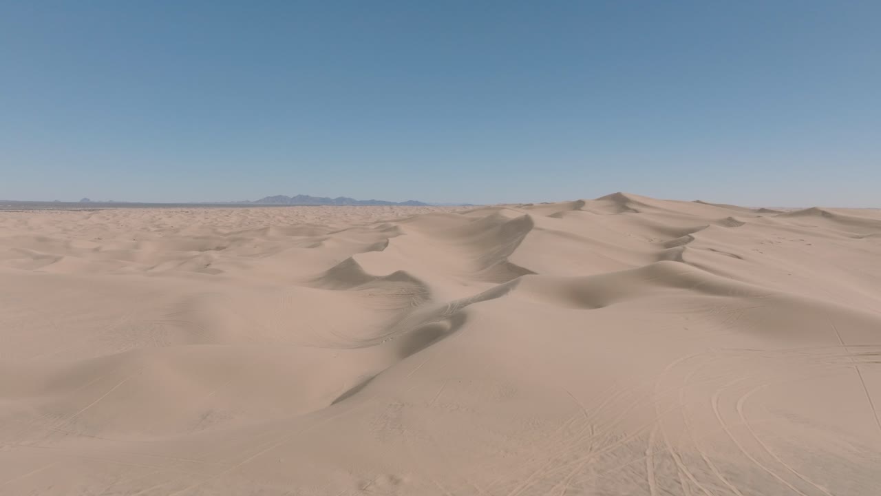 drone volando sobre un vasto paisaje de dunas de arena en el sur de california, cielo azul por delante y arena suave por debajo