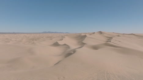 Drone-Volando-Sobre-Un-Vasto-Paisaje-De-Dunas-De-Arena-En-El-Sur-De-California,-Cielo-Azul-Por-Delante-Y-Arena-Suave-Por-Debajo