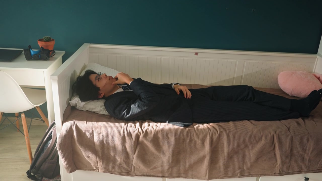 Young person lying on daybed, contemplative student unwinding after study teal wall backdrop, white daybed, pink heart pillow, side table with plant, backpack on floor, soft windowlight falling