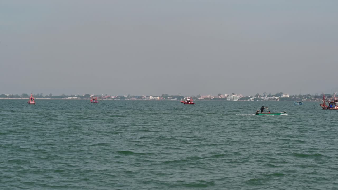 쾌속 어선은 오른쪽으로 향하고 다른 사람들은 햇살 좋은 날 정박해 있으며 배경은 태국 촌부리에 있는 파타야 시입니다.