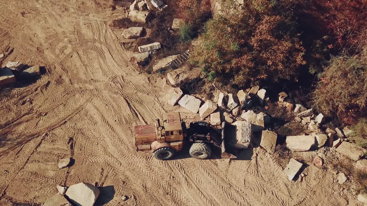 yellow bulldozer with a bucket is carrying a large stone near a sand quarry. Camera motion down. Close-up
