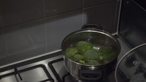 Bowl-of-broccoli-florets-dumped-into-cook-pot-of-hot-water-on-stove