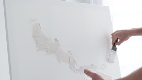 close up the artist applies a plaster base on a white canvas close up the artist applies a plaster base on a white canvas the artist works in his modern studio modern abstract art