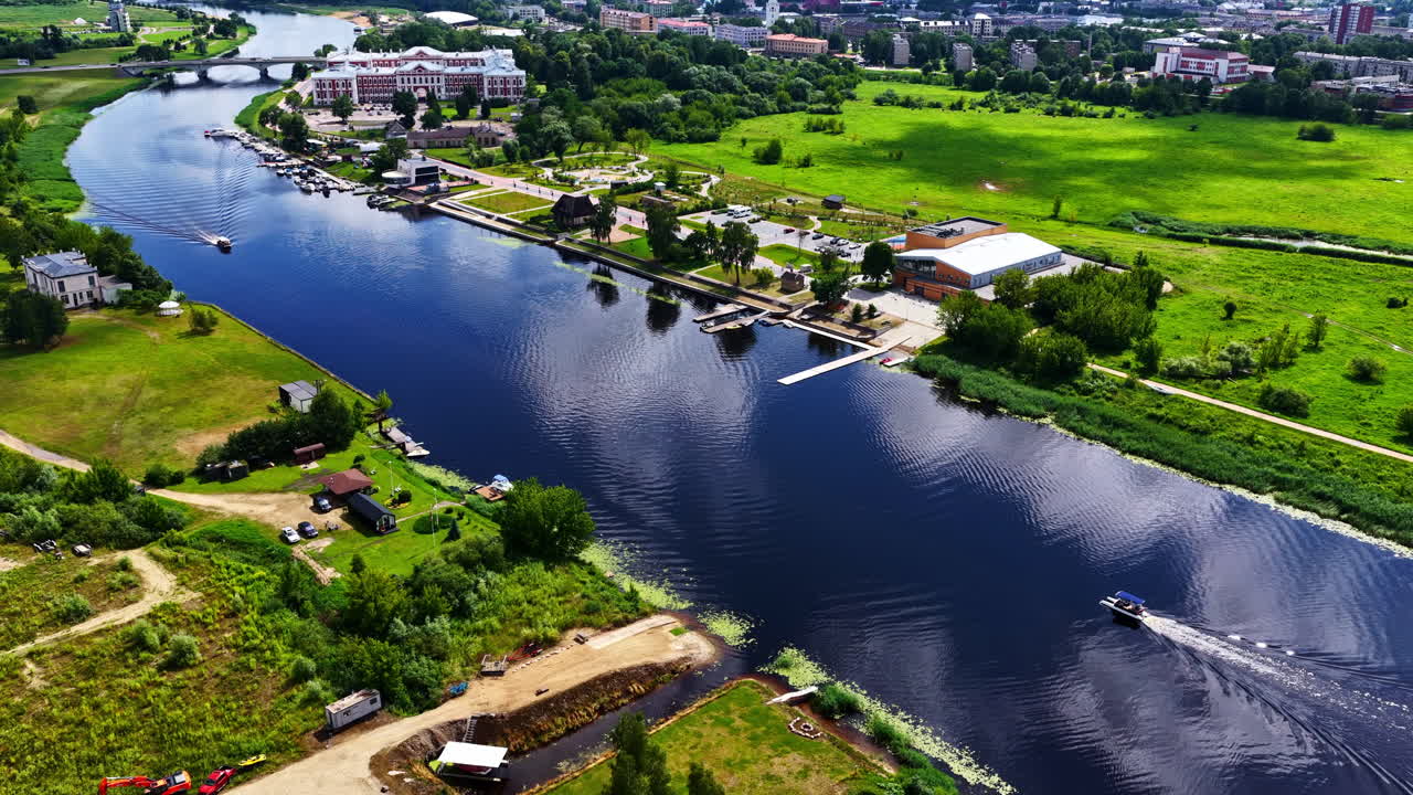 A dynamic aerial shot with tilt-up parallax motion reveals the city of Jelgava, Latvia, starting on the Lielupe River and rising to show the Jelgava Palace and bridge