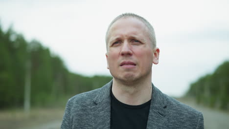 close-up view of a man in glasses and a gray jacket standing on a railway track, removed his glasses with one hand while looking thoughtfully into the distance, with a blurred background