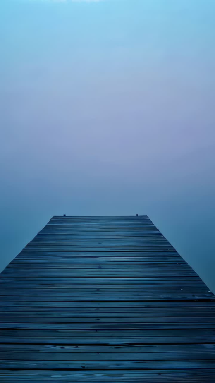 Vertical video: Shifting fog causing wooden dock extending over calm water with planks and bollards