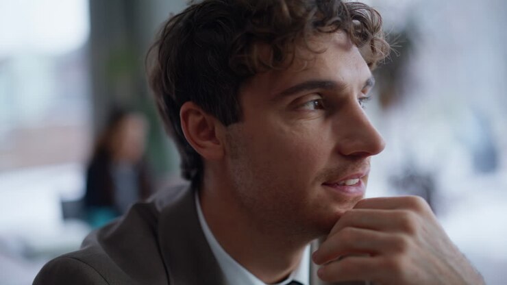 Dreamy businessman holding pen looking distance having break in office closeup