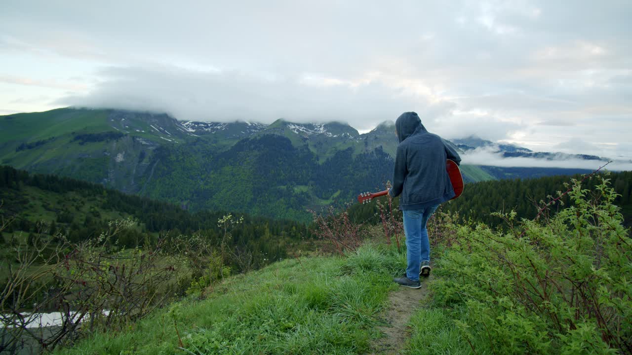 A man is playing the guitar at the top of a mountain under a moody sky