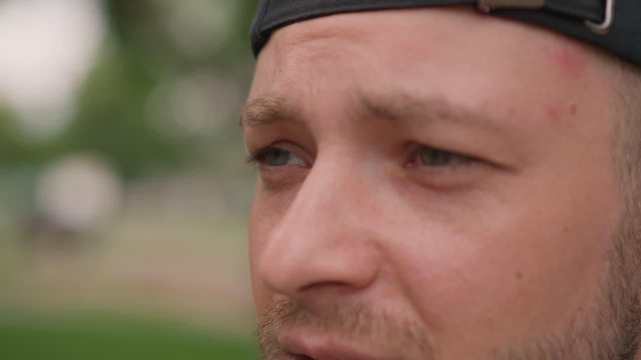 primer plano de un hombre blanco sonriendo en un parque, retrato espontáneo con gorra que muestra una sonrisa gradual y una risa cálida; los fotogramas sugieren el saludo de un amigo, el ánimo de un entrenador callejero, la celebración de un skater o un festival de fin de semana
