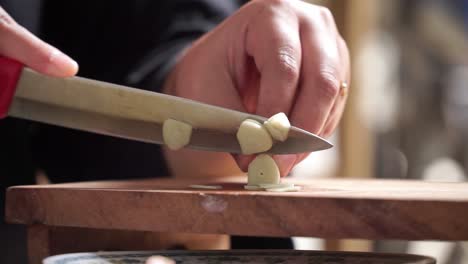 hands chopping garlic with a knife, a close-up view in a warmly lit kitchen atmosphere