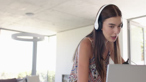 teenage caucasian girl with long brown hair is focused on her laptop, wearing headphones