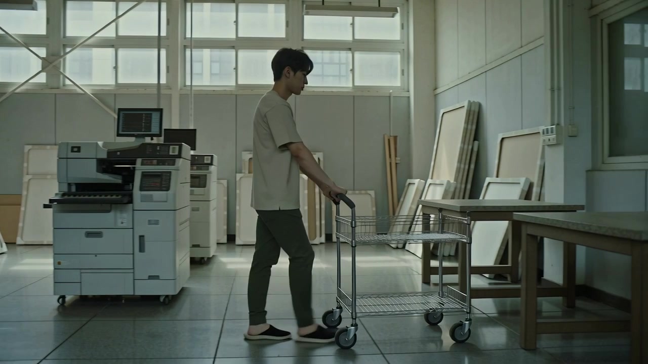 Entering left, man pushing empty cart across studio to worktable to load canvases