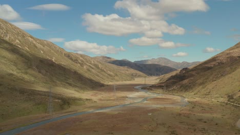 aerial view of a valley with a narrow winding river and some high voltage towers in new zealand