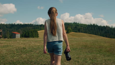 young girl photographer walking with camera young photographer walking with camera on grass hill girl watching at beautiful landscape and amazing nature view spending leisure time outdoor slow motion front view