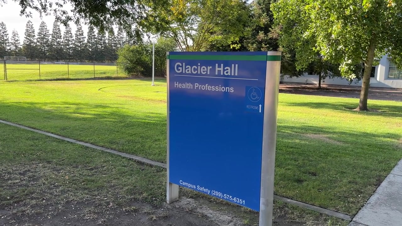 Scena mattutina luminosa in un campus con l'insegna Glacier Hall Health Professions circondata da un prato verde, alberi frondosi e vialetti moderni, catturata con una luce solare naturale e nitida
