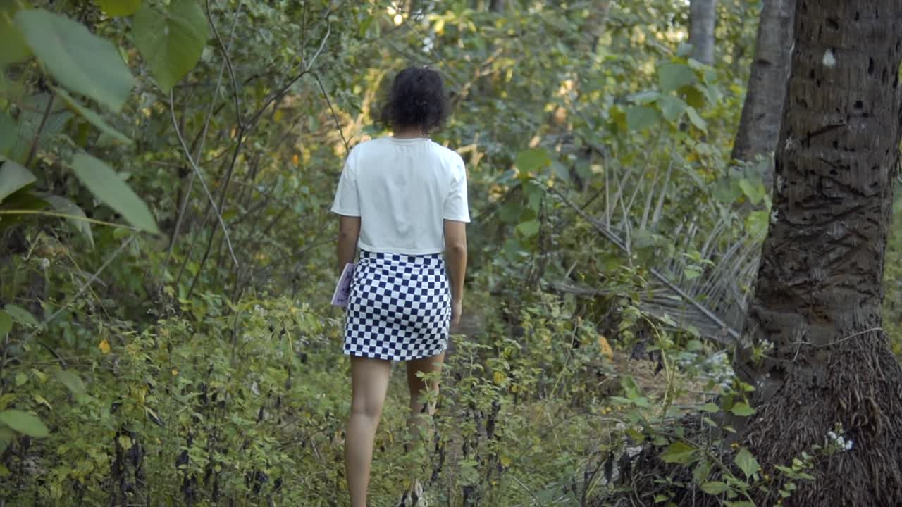 toma cinematográfica en cámara lenta de una modelo con una camisa blanca y una falda con patrón de tablero de ajedrez en blanco y negro en la selva tropical de goa, moda, slomo