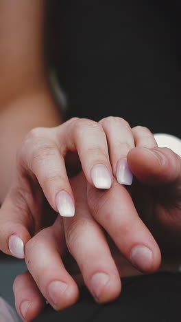 cu shot, slow motion: gentle young lady in lacy wedding dress puts hand on groom wearing black suit fingers sitting together extreme close view