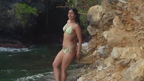 peaceful woman in a bikini standing on trinidad's cliffside with a beach view behind her