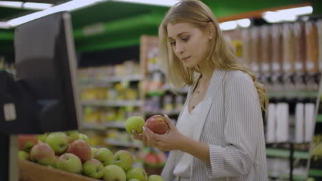 joven atractiva eligiendo una manzana en el mercado de frutas y verduras del supermercado