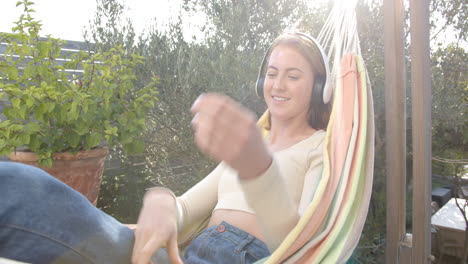 relaxing in hammock, woman wearing headphones enjoying music in backyard garden