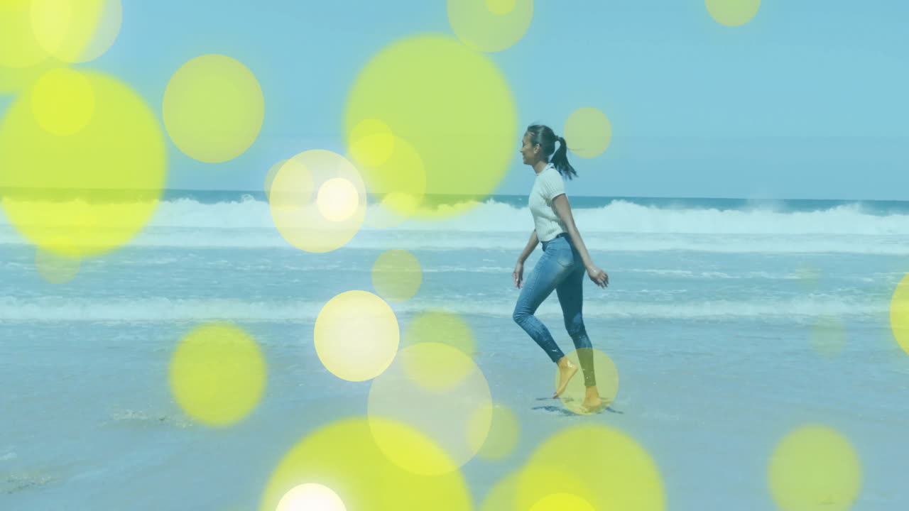 woman walking on wet sandy beach, with animated yellow bokeh highlighting travel marketing concept