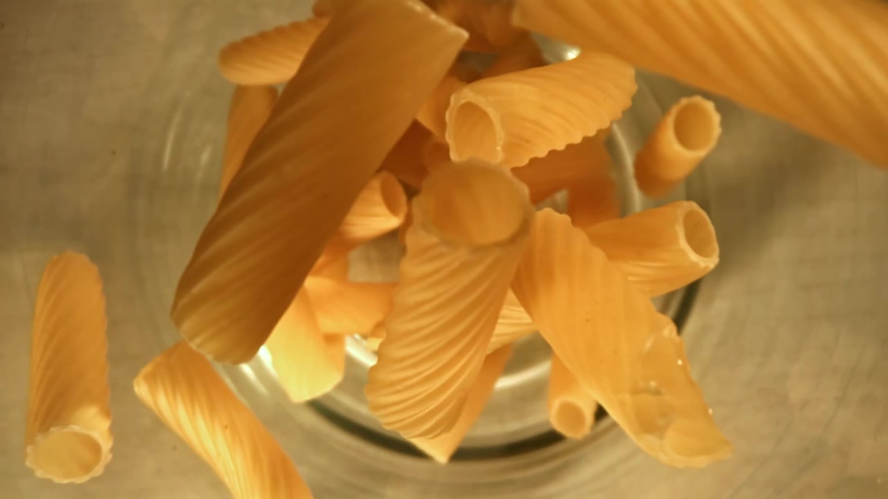 Rigatoni secchi che cadono in una ciotola di vetro