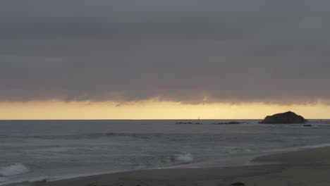 overcast sky over a calm ocean at sunrise. distant rock formations and soft waves meet a glowing horizon for a moody, cinematic coastal scene.