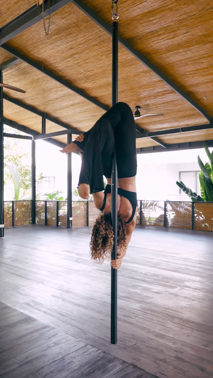 Donna atletica che esegue un'inversione di pole fitness aereo in studio