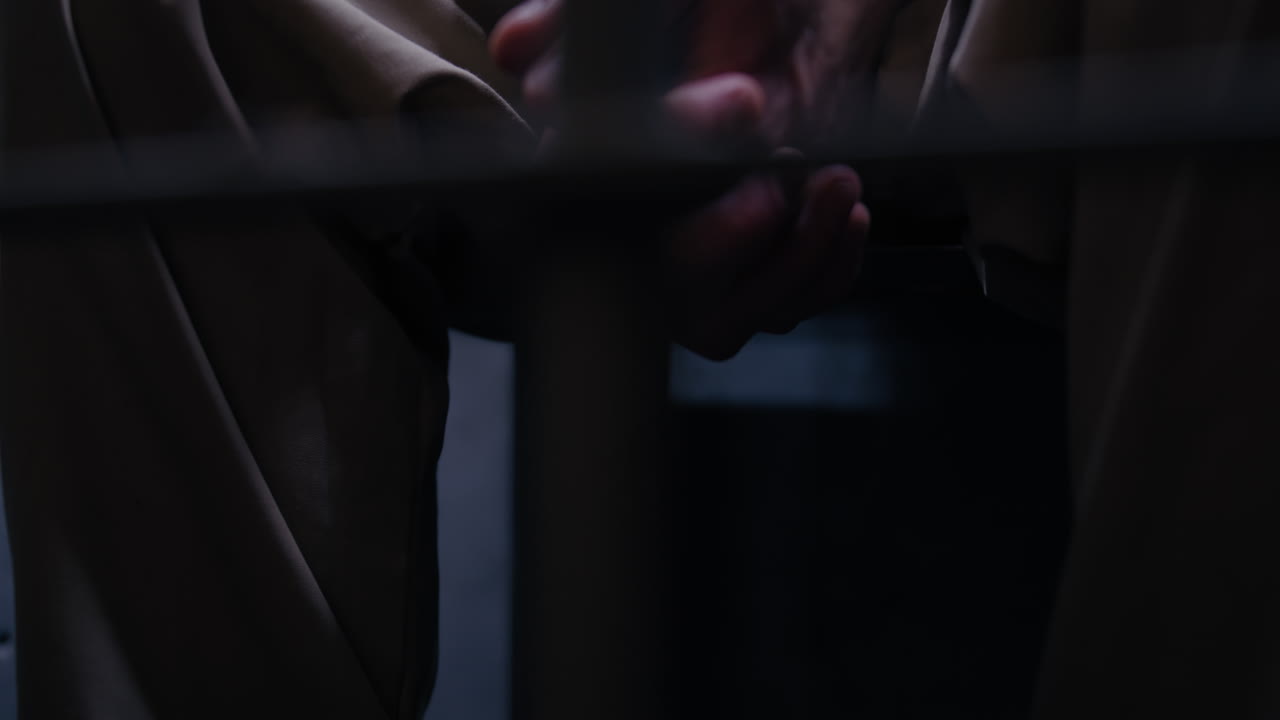 Close-up of sitting prisoner's hands and legs as the camera tracks right while panning left